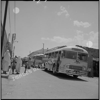 En ville, deux bus venus récupérer des enfants stationnent en attendant le départ pour les emmener au Camp des chasseurs du 8e RIM. [légende d'origine]