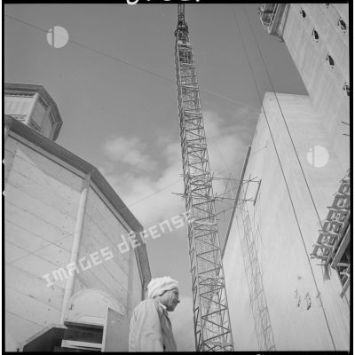 [Vue en contre-plongée d'un homme devant un silo, une grue et un bâtiment en construction sur les docks coopératifs de Saïda.]