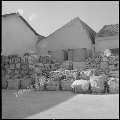 [Papeterie d'Aïn-el-Hadjar. Vue sur des matériaux conditionnés et stockés à l'extérieur, devant des bâtisses.]