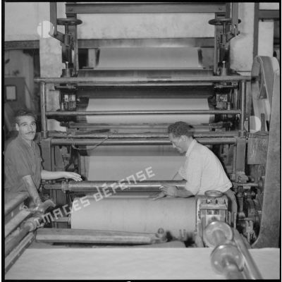 [Papeterie d'Aïn-el-Hadjar. Deux ouvriers travaillent avec une machine munie de cylindres et utilisée pour la fabrication du papier.]