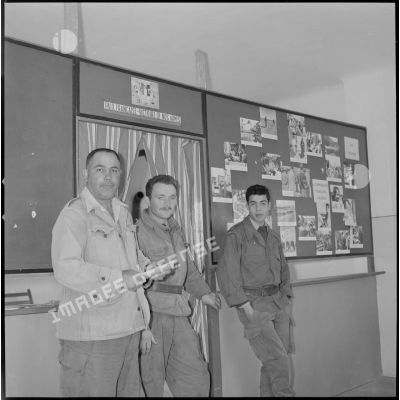 [Trois hommes posant dans le hall d'information de Saïda avec à gauche, un interprète officiel et à droite, un nouvel aspirant du commando Cobra.]