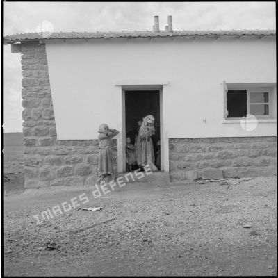 [Vue d'une bâtisse nouvellement construite dans le centre de regroupement de la ferme Cazorla. Une femme balaye le pas de sa porte.]