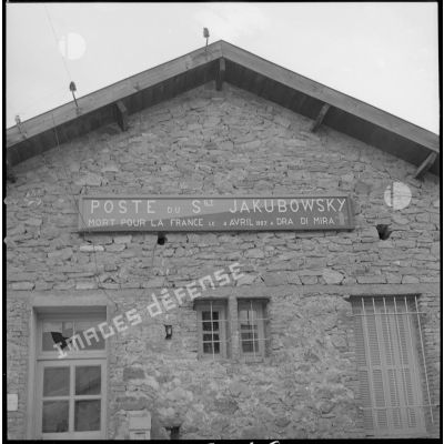 [Vue sur la façade d'une bâtisse du cantonnement de Sidi Maarouf portant l'inscription "Poste du sergent Jakubowsky mort pour la France le 4 avril 1957 à Dra di Mira".]