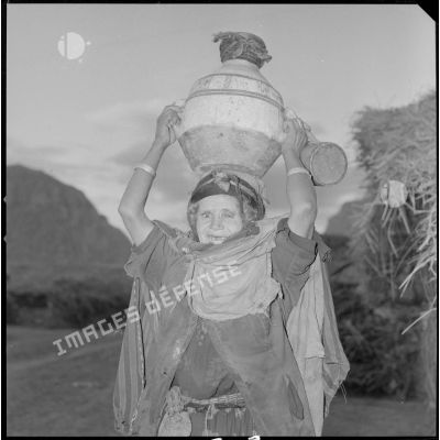 [Portrait d'une femme kabyle âgée portant une jarre sur la tête.]
