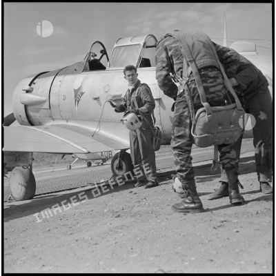 [Aérodrome de Nazereg-Flinois. Le photographe Arthur Smet, de dos, s'équipe d'un parachute pour un vol de reconnaissance à bord d'un avion North American T-6 piloté par un lieutenant, de face, de l'escadrille d'aviation légère d'appui (EALA).]