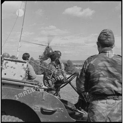 [Opération avec le commando Georges dans le secteur de Fenouane, près de la ferme Garrigues. Capitaine, accoudé au volant d'un véhicule de type jeep, en communication radio. Hélicoptère de type Sikorsky H-34 en vol.]