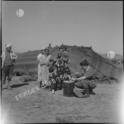 [Distribution de lait auprès d'une famille de nomades algériens par un soldat à Aïn Shkouna.]