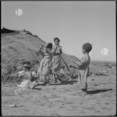 [Enfants jouant des percussions et dansant dans un camp de regroupement de nomades à Aïn Skhouna.]