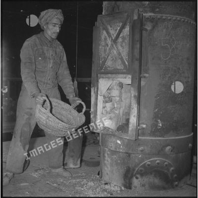 [Ouvrier algérien versant du charbon dans le four d'une fonderie près de Saïda.]