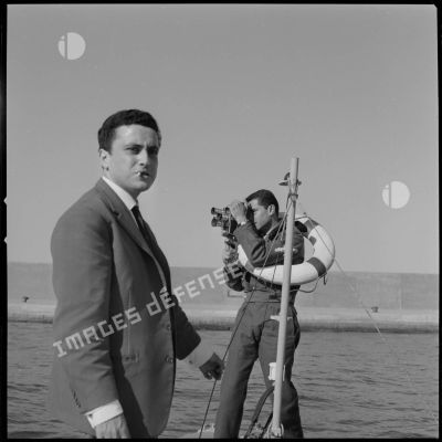 [Un journaliste et un caméraman aux Armées se tenant sur une embarcation à Oran.]