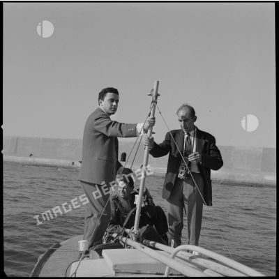 [Un caméraman aux Armées, un photographe et un journaliste tenant le mat d'une embarcation à Oran.]