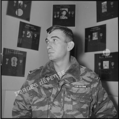 [Portrait d'un sergent devant le mur d'honneur des Cobra à la ferme Rouge.]