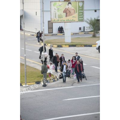 Des ressortissants évacués se dirigent vers leur avion pour l'embarquement sur l'aéroport de Tripoli (Libye), passant près d'une affiche représentant le colonel Kadhafi.