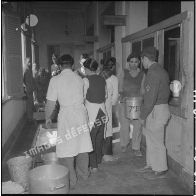 Du personnel vitenamien s'occupe de récipients remplis d'aliments dans un couloir à l'hôpital militaire Lanessan.