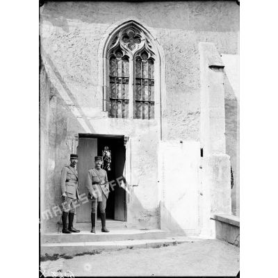 A la porte de l'église d'Essey-lès-Nancy, deux officiers sont photographiés à côté d'une pierre tombale. [légende d'origine]