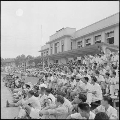 Dans les gradins du stade Mangin, les spectateurs regardent le match de football opposant l'équipe de Nam-Hoa à la sélection Nord-Vietnam.
