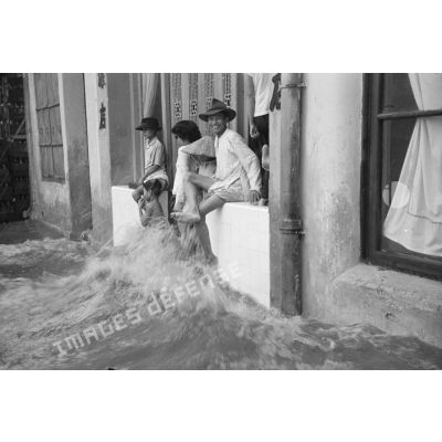 Une femme et des enfants devant une habitation d'une rue inondée par les pluies.