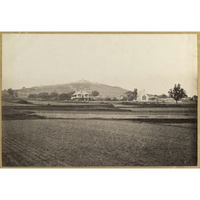 [Chine, 1870-1890. Vue d'une plaine avec des bâtiments de style colonial dont une église. A l'arrière-plan, sur une colline, un ouvrage fortifié].
