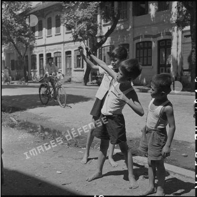 Dans une rue, des enfants tirent à la fronde sur des oiseaux.