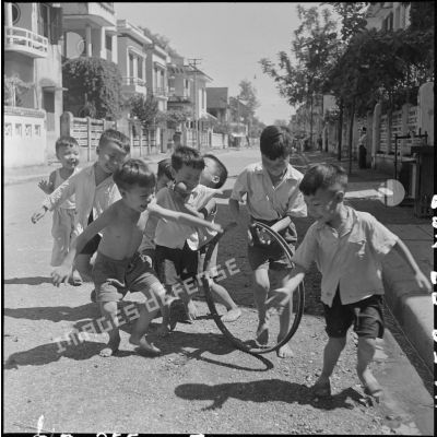 Enfants jouant avec une vieille jante de cycle dans une rue.