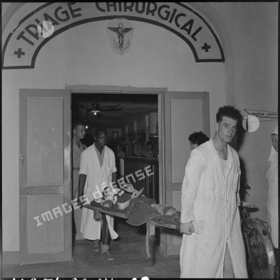 Brancardiers transportant, hors de la salle de triage de l'hôpital militaire Lanessan, un soldat blessé, évacué de Diên Biên Phu.