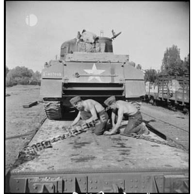 En gare de Boufarik, des soldats français arriment sur un wagon porte-chars un char moyen sherman M4 A4 américain, destiné au 5e RCA (régiment de chasseurs d'Afrique) de la 1re DB (division blindée).