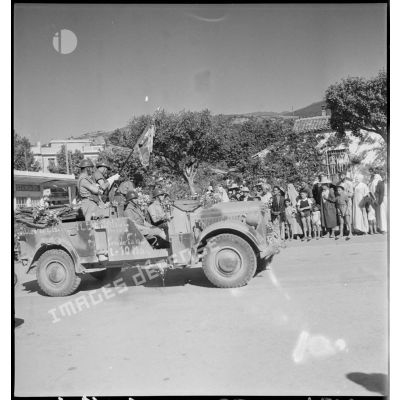 Un véhicule de liaison allemand Kfz-15 pris à l'ennemi par le 65e RAA (régiment d'artillerie d'Afrique) pendant la campagne de Tunisie, à bord duquel l'étendard du régiment est embarqué, défile dans une rue de Blida.