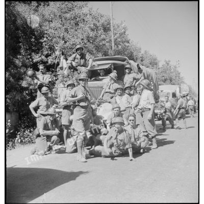 Portrait de groupe d'artilleurs du 65e RAA (régiment d'artillerie d'Afrique), de retour de la campagne de Tunisie, posant devant une colonne de véhicules sur une route menant à Blida.