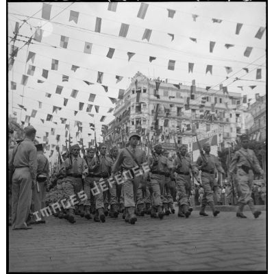 Défilé de tirailleurs du 1er RTA (régiment de tirailleurs algériens) lors du 14 juillet 1943 dans une rue pavoisée de la ville.