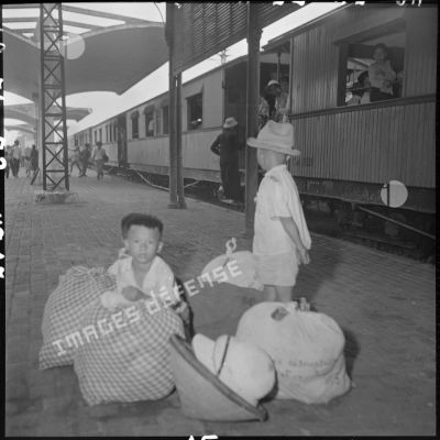 Sur un quai de la gare d'Hanoï, des enfants gardent des bagages.