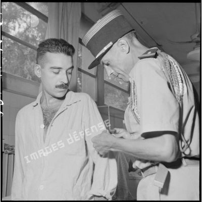 Le colonel Lalande (à droite) accroche un losange de bras sur la chemise d'un homme hospitalisé à l'hôpital militaire Lanessan.