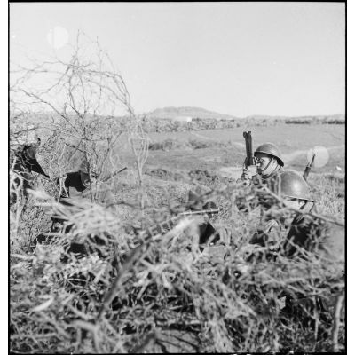 Des servants d'un canon antichar américain de 37 mm sont camouflés dans la végétation pendant que le chef de pièce observe l'objectif avec des jumelles périscopiques.