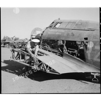 Un mécanicien de l'armée de l'Air française démonte les plans d'un avion de chasse Hawker Hurricane sur une chaîne de maintenance. Sur le fuselage, les marques des victoires de l'appareil.