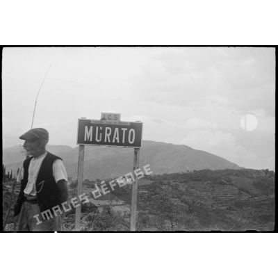 Un civil corse se tient près du panneau indacteur de la ville de Murato.