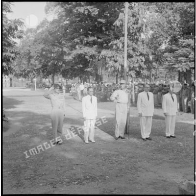 Le général de Castries, M. le Gouverneur du Nord-Vietnam, le général Cogny, M. Bordaz et M. Compain devant un monument aux morts dans un square.