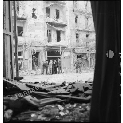 Des civils discutent devant un immeuble endommagé de la rue d'Isly après le bombardement allemand visant l'aérodrome Maison-Blanche à Alger, dans la nuit du 20 au 21 novembre 1942.