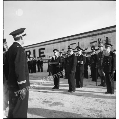 Lors d'une cérémonie, un capitaine de vaisseau lit les citations accompagnant les Croix de guerre remises aux commandants des sous-marins Casabianca, Le Glorieux et Marsouin.