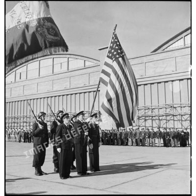 Pendant la cérémonie sur l'aérodrome de Maison-Blanche à Alger en l'honneur du GC II/5 La Fayette, le lieutenant Pierre Le Gloan, porte-drapeau présente symboliquement le drapeau des Etats-Unis. Au premier plan, le drapeau de la 5e escadre aérienne.