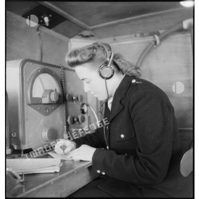Instruction pratique de TSF dans une remorque d'écoute pour une élève de l'école des transmissions des personnels féminins de l'armée de l'Air : l'écoute en station, transcription d'un message.