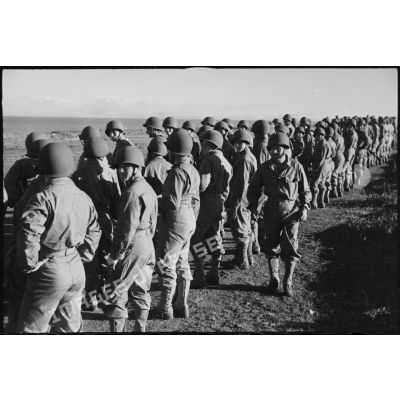 Rassemblement sur les rangs de soldats de la 2e division blindée (2e DB), équipés de tenues américaines, lors d'une inspection de la division.