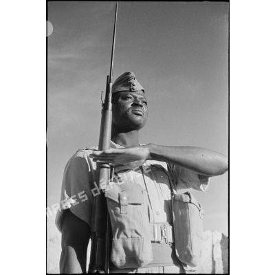 Portrait d'un tirailleur sénagalais, équipé à la britannique, au présentez-armes lors d'une inspection.