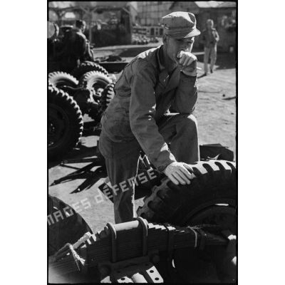 Portrait d'un chef monteur américain, en tenue de travail, appuyé à un pneu.
