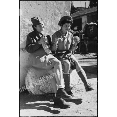 Assises sur un rocher, deux volontaires féminines conductrices à la 521e compagnie sanitaire tricotent.