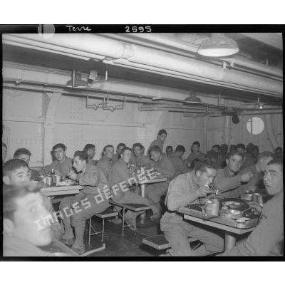 Des soldats français mangent à l'équipage d'un bâtiment de transport américain d'hommes et de matériel.