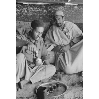 En Libye, sous une tente, deux aviateurs partagent un repas avec des bédouins.