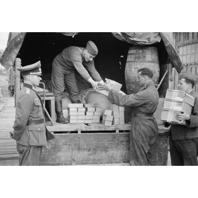 Sous la surveillance d'un officier du magasin d'approvisionnement, le chargement de tabac dans un camion de l'armée de l'air allemande.