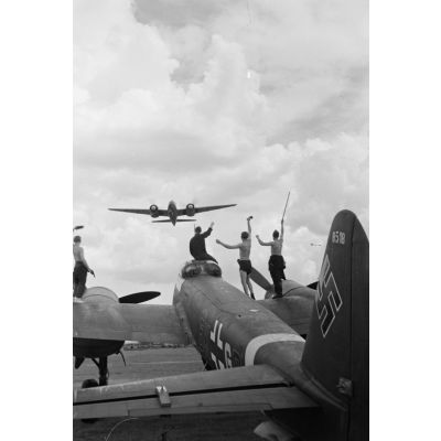 Des mécaniciens du Kampfgeschwader 3 Blitz, debout sur le Junkers Ju-88 codé 5K+GP, saluent l'équipage d'un bombardier qui survole le terrain d'aviation.