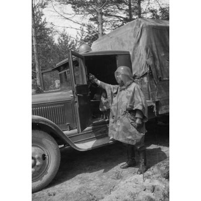 Devant un camion ZIS d'origine soviétique, un fantassin de la Luftwaffe équipé d'une moustiquaire et d'un poncho.