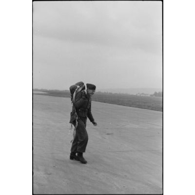 Sur le tarmac d'un terrain d'aviation norvégien, un pilote de planeur du Luftlandegeschwader 1 portant son parachute l'épaule.