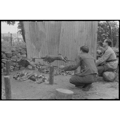 Des aviateurs de la Luftwaffe surveillent la cuisson de la viande pour méchoui organisé au sein d'une unité de reconnaissance de l'armée de l'Air allemande (Aufklärungsgruppe).